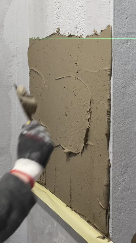 Master tiler applies tile adhesive with a spatula to the wall Stock Footage 317902275