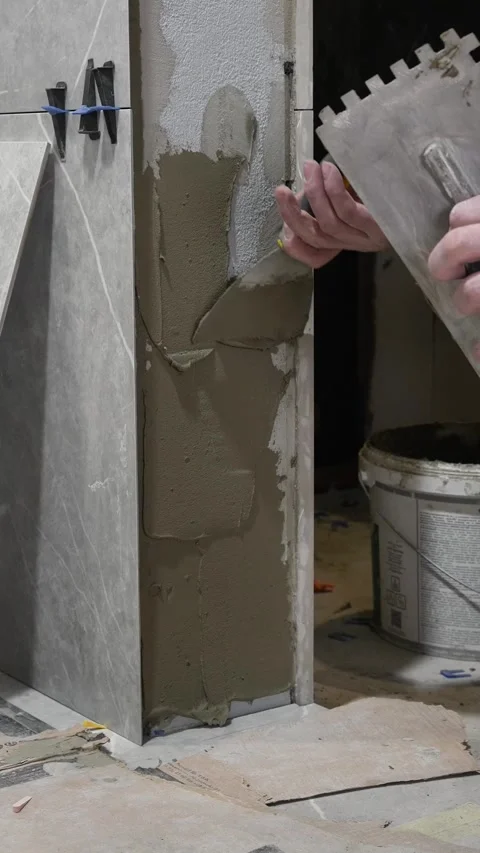 Master tiler applies tile adhesive with a spatula to the wall Stock Footage 317902382