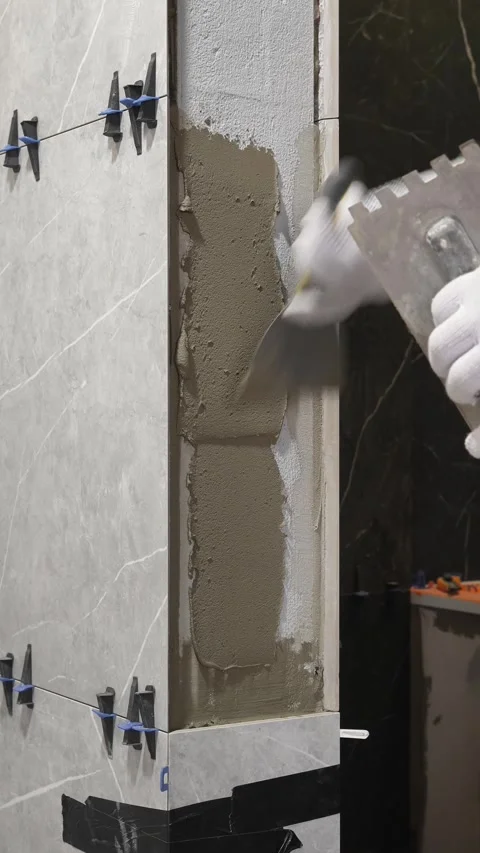 Master tiler applies tile adhesive with a spatula to the wall Stock Footage 317902398