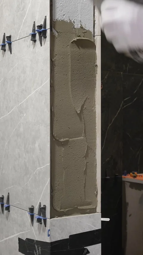 Master tiler applies tile adhesive with a spatula to the wall Stock Footage 317902407