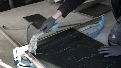 Master tiler cuts and breaks black porcelain tiles on a dry tile cutter Stock Footage 306019151