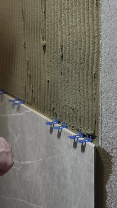 A master tiler pushes a tile leveling system under the tile Stock Footage 317902330