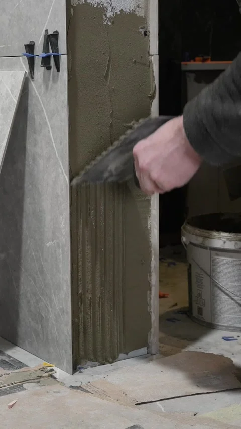 A master tiler removes tile adhesive from a wall with a notched trowel Stock Footage 317902381