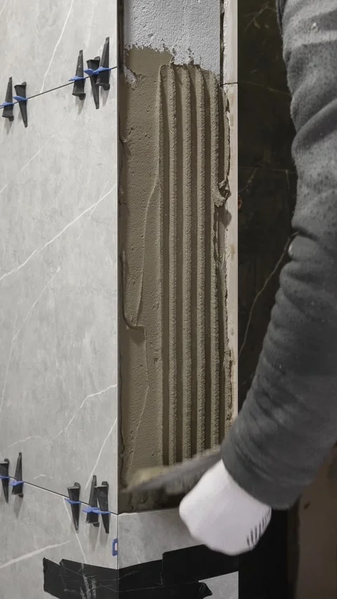 A master tiler removes tile adhesive from a wall with a notched trowel Stock Footage 317902401