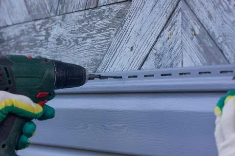 Master twists siding on the wall with a screwdriver Stock Photos