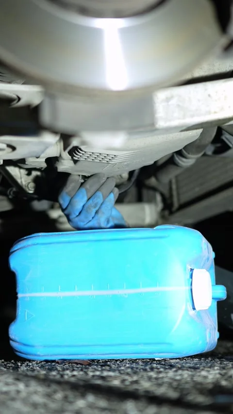 The master unscrews the bolt and drains the black used oil from the car into a b Stock Footage 320128211