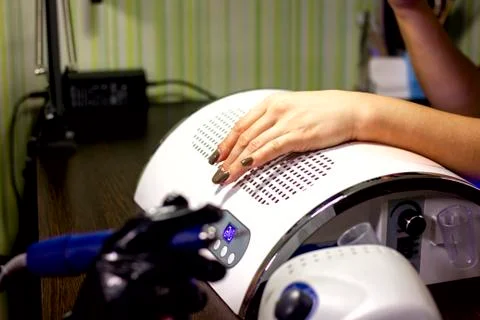 Master uses a machine and a cutter to process the girl`s nails Stock Photos