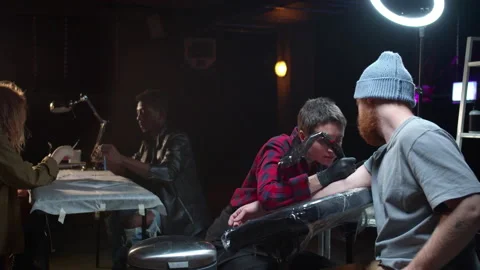 The master uses a tattoo machine. Customers are waiting at the table Stock Footage 131064681