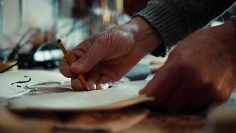 Master using a pencil to draw on the front panel of the unfinished violin Stock Footage 167112472