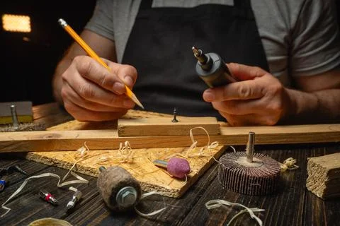 Master is using a tool to shape a small piece of wood on a workbench. They .. Stock Photos