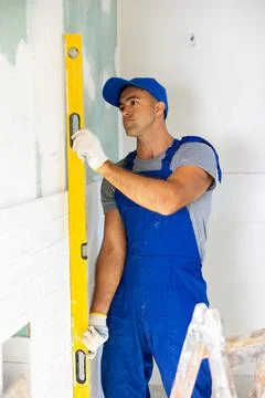 Master wearing work clothes checking vertical of installing tiles using building 写真素材