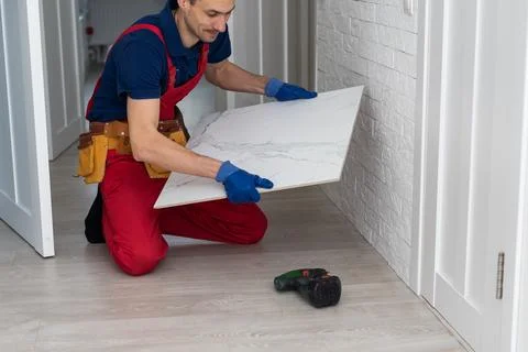 Master is wearing work clothes, is checking horizon of installing tiles, using Stock Photos