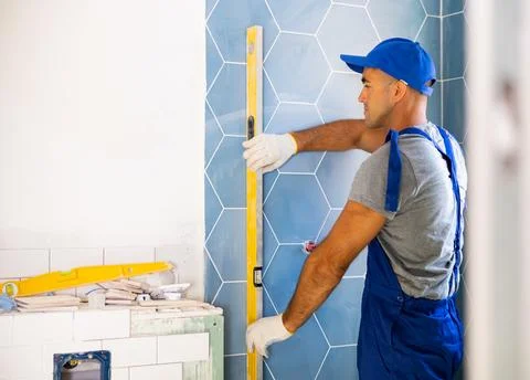 Master wearing work clothes checking vertical of installing tiles using building 写真素材