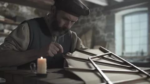 Master winding thread around an ornithopter wing tip next to a burning candle Vídeo Stock 339632742