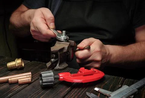 A master works on a plumbing project in a workshop. They use a wrench to tigh Stock Photos