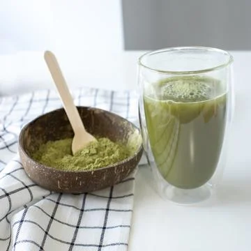 Matcha green tea in a double-walled glass cup with a bowl of powder. Stock Photos