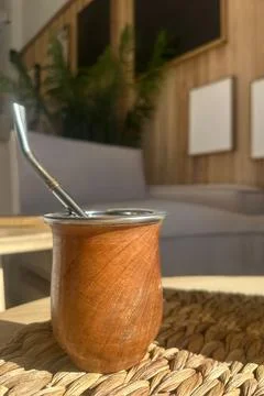 Mate cup with straw placed on a table in a warm, neutral-toned home interior.  Stock Photos