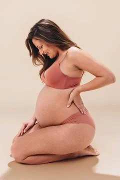 Maternal love: Pregnant woman smiling at her baby bump in a studio Stock Photos