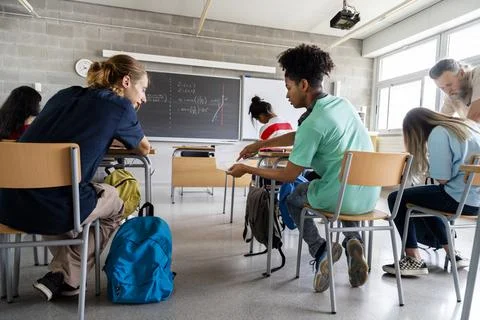 In math class two male high school students passing a note while male teacher Stock Photos