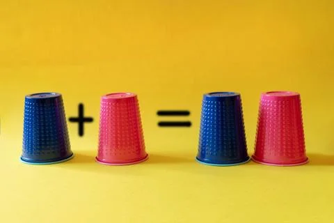Math exercise: one plus one equals two. Multi-colored blue and pink plastic cups Stock Photos