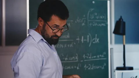 Math teacher explaining concepts near chalkboard during classroom lecture Stock Footage 313493256