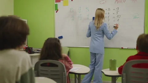 Math teacher quizzing pupils and writing equation on board in classroom lesson Stock Footage 333586802