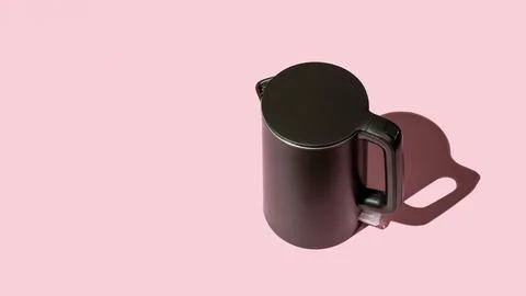 Matte black kettle casts shadow on a pink background. Stock Photos