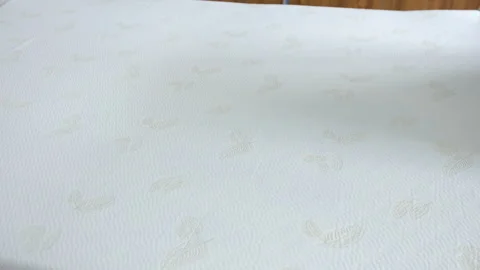A mattress surface featuring a soft, white fabric with subtle embossed leaf Stock Footage 314427880