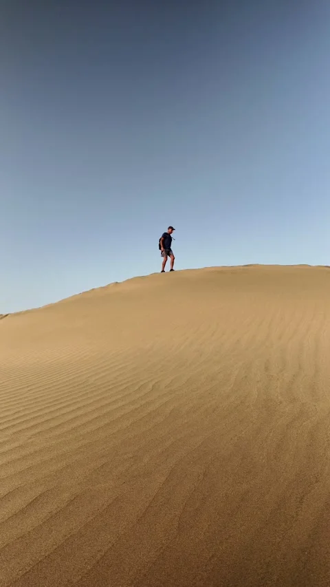 Mature active man walking along a sand dune in the desert Stock Footage 345093139