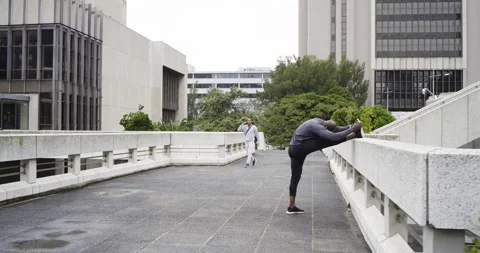 Mature African American man using railing for lunges on terrace while man Stock Footage 340964199