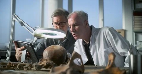 Mature archaeologist uses tablet computer and talks to colleague Stock Photos