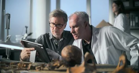 Mature archaeologist uses tablet computer and talks to colleague Stock Photos