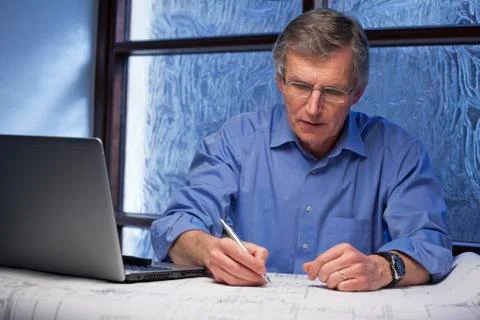 Mature architect or engineer working from home at a desk with laptop an plan Stock Photos