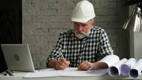 Mature architect working on blueprint, using laptop Stock Footage 231680799