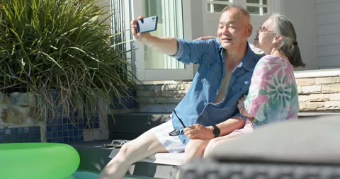 Mature Asian couple posing at pool edge while man holding smartphone and Stock Footage 344331278