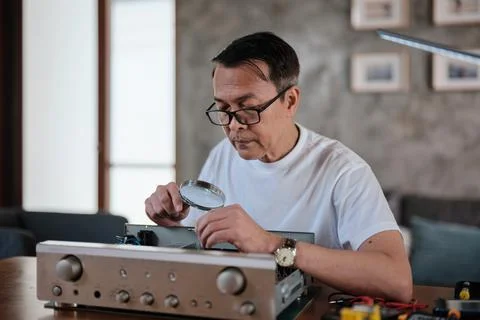 Mature Asian man disassembling audio equipment for repair, home DIY workshop. Stock Photos