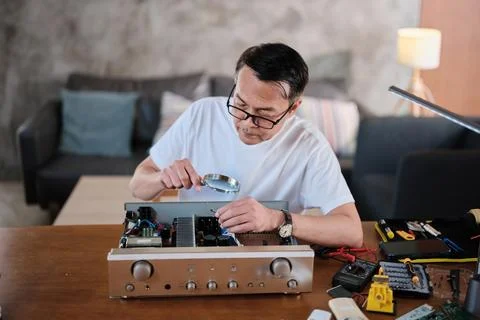 Mature Asian man disassembling audio equipment for repair, home DIY workshop. Stock Photos
