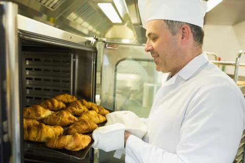 Mature baker putting some croissants into an oven Stock Photos