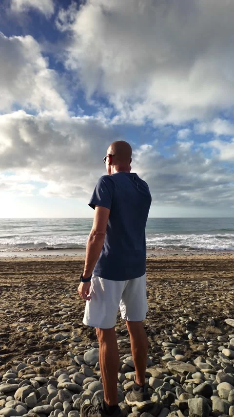 Mature bald man walking alone on a pebble beach Stock Footage 346177801