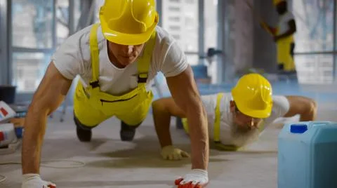 Mature builders in uniform doing pushups during break at work site Stock Photos