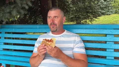 Mature Caucasian man eats fast food, a tortilla with meat and vegetables on the Stock Footage 281533653