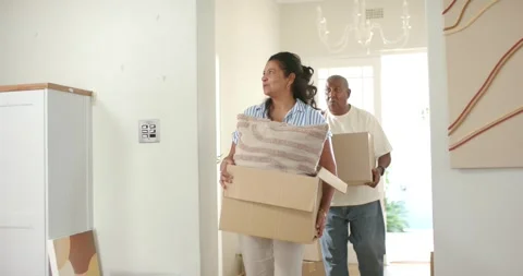 Mature couple carrying moving boxes and pillow, entering entry hall, eyeing Stock Footage 340974580