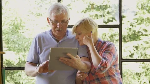 Mature couple chatting on tablet computer by window at home Stock Footage 78764293
