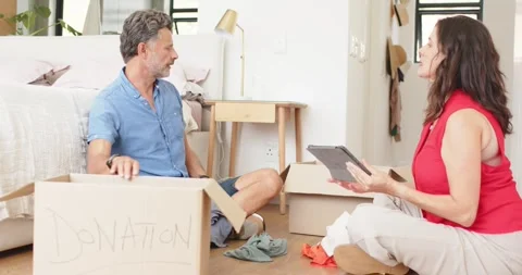 Mature couple checking tablet list and packing DONATION box on bedroom floor, Stock Footage 345072280