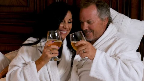 Mature couple clink glasses in white robes Stock-Footage 94267553
