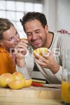 Mature couple eating grapefruit in kitchen, smiling, close-up Stock Photos