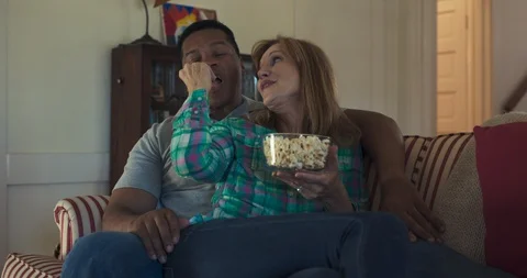 Mature couple eating popcorn while sitting back on the couch watching a movie Stock Footage 116898061
