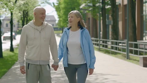 Mature couple holding hands while walking together in the street. Rear view of Stock Footage 219855942
