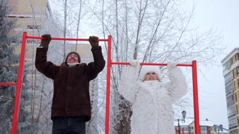 Mature couple performs pull-ups on bars on winter playground Stock Footage 330106690