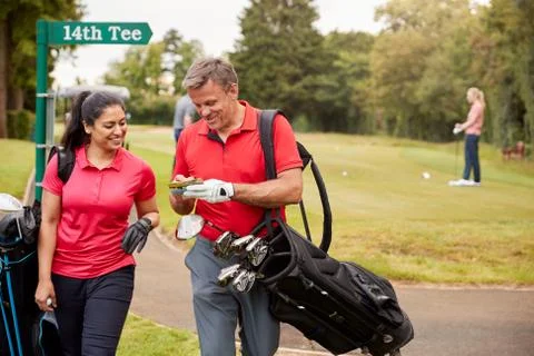 Mature Couple Playing Round Of Golf Carrying Golf Bags And Marking Scorecard Fotos de archivo